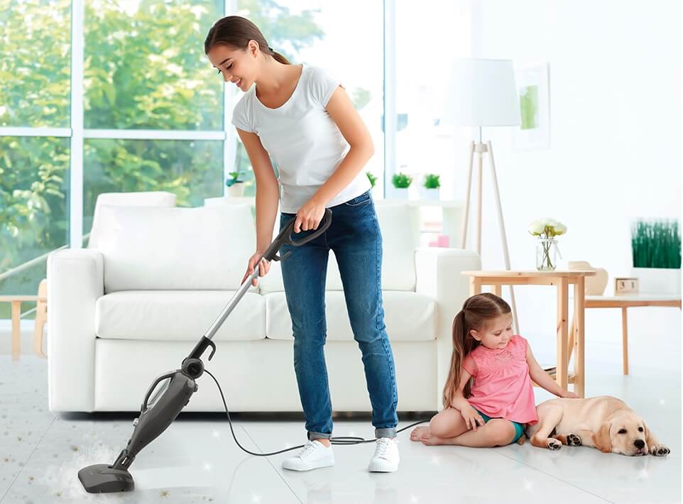 Limpieza de la casa. La chica sostiene un limpiador de vapor eléctrico, que  limpia el extracto de la cocina, la superficie, con vapor húmedo caliente.  Limpieza de la superficie Fotografía de stock 